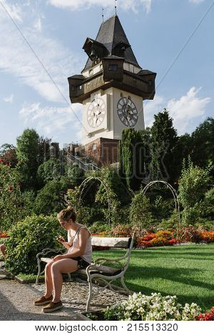 Graz, Austria - August 11, 2017: Woman sitting on bench at Uhrturm clock tower in Graz