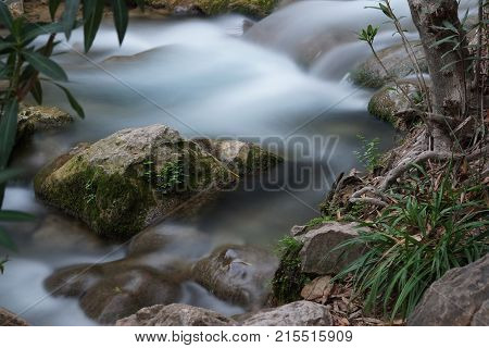 A Small Current Creek With Rapids And A Stone With Moss Protruding From The Water
