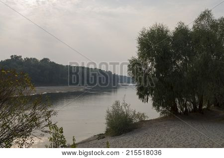 Wide river flowing across green forest. Fall. Evening. Reflections of trees in the calm water. Sundown