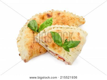 One whole and half of the baked calzone - closed type of pizza that is folded in half decorated with basil twigs on a white background
