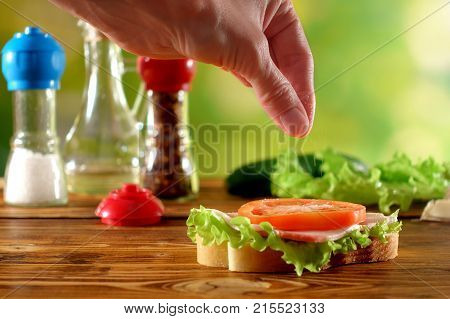 Woman's hand salts sandwich with tomato and salad