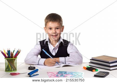 Cute cheerful pupil sitting still at the desk, surrounded with stationery.