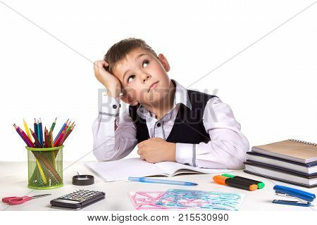 Excellent pupil thinking over the puzzle sitting at the studing desk with white background.