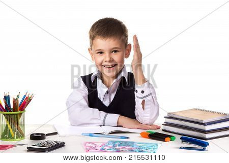 Smiling excellent pupil with hand up sitting at the table on the white background.
