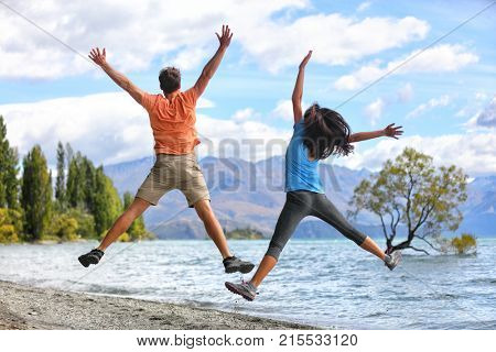 New Zealand tourists couple jumping of happiness at Wanaka Lone . Happy young people doing funny jump of joy sightseeing traveling in summer adventure destination. Woman and man.