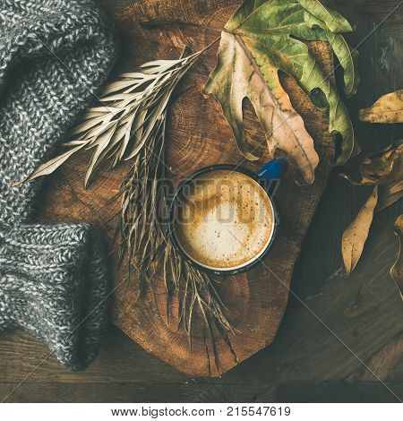 Autumn or Fall morning coffee concept. Flat-lay of arm knitted woolen grey sweater, wooden tray, mug of coffee and yellow fallen leaves over dark rustic wooden table background, top view, square crop