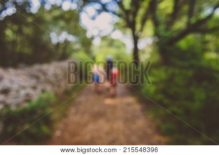 Family hiking on country road with rock fence and woods. Mother and daughters are trekking through rough terrain on island Silba Croatia. Intentionally blurred and defocused for background.