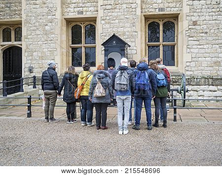 London, UK: November 21, UK: A crowd of tourists crowd around a soldier wearing a bearskin on guard in the Tower of London.