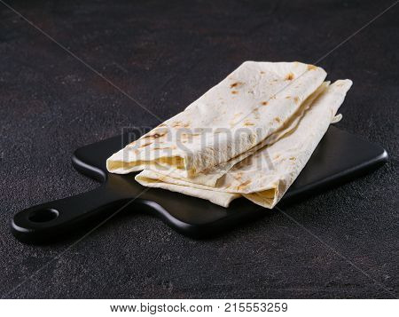 Armenian flat bread lavash. Pita bread on black cutting board over black cement background. Copy space.