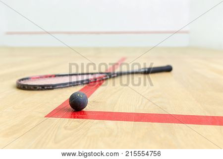 squash racket and ball on the wooden floor. Racquetball equipment on the court and wall with red lines on the background. Photo with selective focus