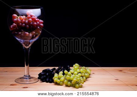 Glass of red win grapes. Grape variety still life. Classic painterly image. Red green and black grape varieties. Summer fruit on farmhouse kitchen table.