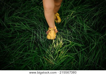 Cute little child legs shod in pretty yellow shoes walking on the fresh green grass
