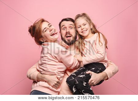 Happy young family with one little daughter posing together on pink studio background