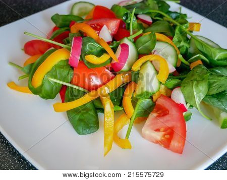 Fresh green vegetable salad with radish tomatoes color peppers on the white plate