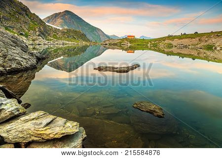The beautiful alpine Caltun lake and colorful mountain shelter with stunning sunset, Fagaras mountains, Carpathians, Transylvania, Romania, Europe