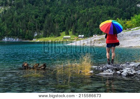 Hiker woman with colorful umbrella near emerald alpine lake, Hinterer Gosausee, Salzkammergut, Austria, Europe