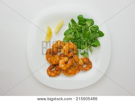 Fried shrimps on a plate. Prawns fried in breading on a white plate with salad and lemon.