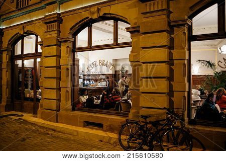 STRASBOURG FRANCE - NOV 21 2017: Tourists and locals drinking a warm coffee or tea inside the Brant Cafe in Strasbourg - view from the street at night