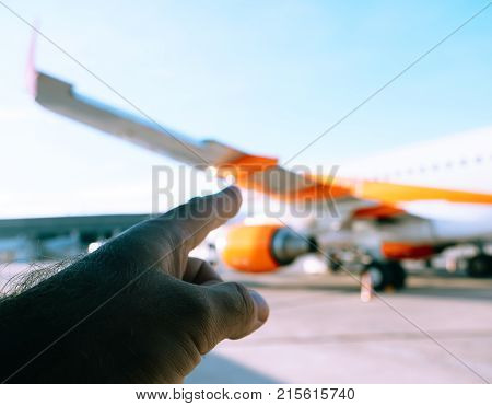 Finger pointing to the orange airplane on the tamrac of a modern airport