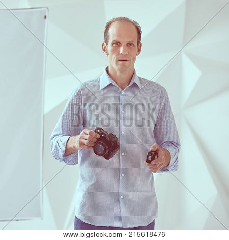 Young professional photographer working in white photo studio, in one hand the camera in another synchronizer, image with vintage toning