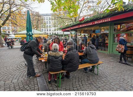 MUNICH, GERMANY - NOVEMBER 16, 2017: Many people eating street-food and drinking at famous Viktualienmarkt on November 16, 2017. Bavaria is famous for its breweries and the Weissbier - wheat beer