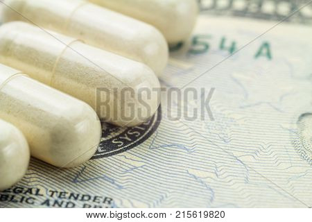 White capsules of glucosamine chondroitin healthy supplement pills on dollar banknote macro image.