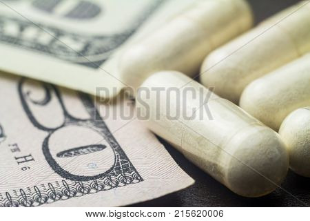 White capsules of glucosamine chondroitin healthy supplement pills on dollar banknote macro image.