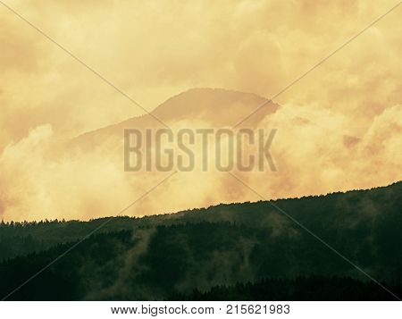 Distant Mountain Range And Heavy Clouds Of Colorful  Mist Above Deep Valleys