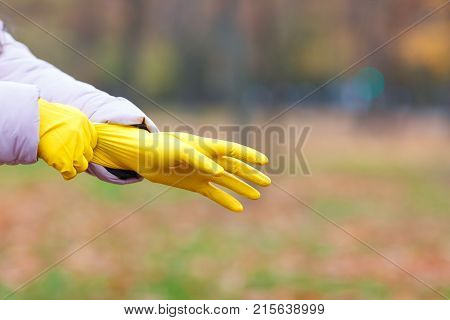 Close-up of a girl in a pink jacket dresses yellow gloves, for cleaning in an autumn park.
