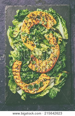 Grilled pumpkin and lettuche salad with white and black sesame and balsamic sauce on slate black board, blue stone background