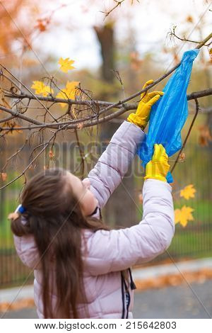 A girl in yellow, rubber gloves, reaches for a branch on a tree to take off the package, which is stuck there.