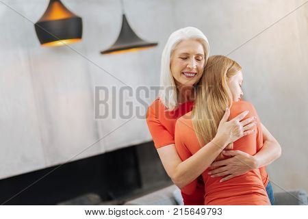 Warm hug. Pleasant happy age woman smiling and hugging her granddaughter while expressing her love for her