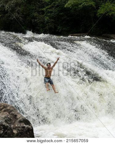 CASHIERS, NORTH CAROLINA - AUGUST 21, 2016: Young adult slides down rocks in Turtleback Falls in Gorges State Park near Cashiers in North Carolina, USA