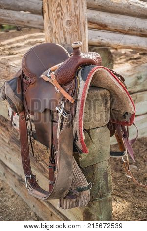 Western riding saddle and horse blanket on wooden corral post after a trail ride