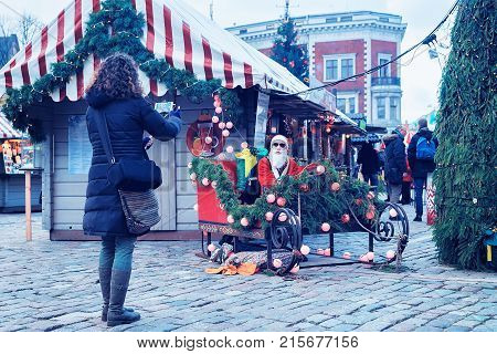 Riga Latvia - December 28 2016: Woman taking photo of Santa Claus in sled on Christmas Market at Dome Square in Riga Old Town in winter