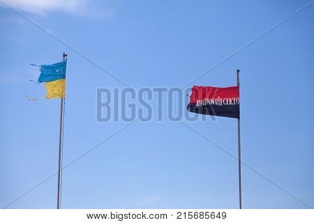 Ukrainian damaged flag and flag of Arms of Ukrainian Nationalists (OUN-UPA) against blue sky