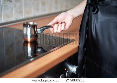 Cooking coffee in traditional copper turkey on a stove - kitchen interior.