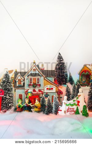 kid gospel choir singing next to Seasons greeting in white Christmas village. Fairytale miniature scenery