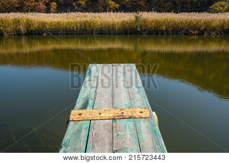 View from the jetty over a calm lake. Small weathered wooden pier.