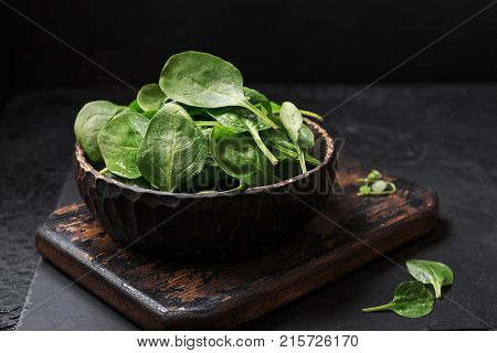 Washed fresh mini spinach in a colander on the old board on the black table