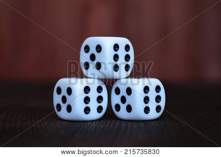 Pyramid of three white plastic dices on brown wooden board background. Six sides cube with black dots. Numbers 5 and 6.