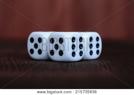 Heap of three white plastic dices on brown wooden board background. Six sides cube with black dots. Numbers 5 and 6.