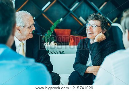 Closeup of four diverse business people discussing ideas and sitting around table in lounge with blurred interior view in background. Two men are sitting back to camera.