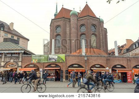 MUNICH, GERMANY - NOVEMBER 16, 2017: People walking in crowd and cycling past stores of famous Viktualienmarkt on November 16, 2017. Bavaria is famous for its breweries and the Weissbier -wheat beer