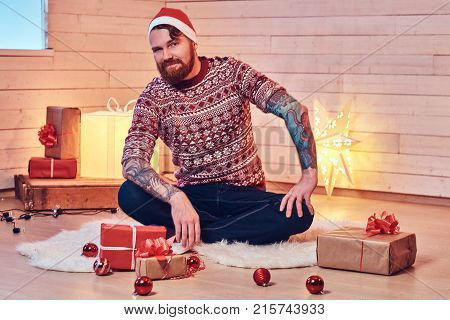Redhead bearded male in Santa hat in a room with Christmas decoration.