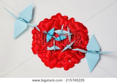 Family of paper cranes from origami in a nest of red hearts concept love caring for the offspring