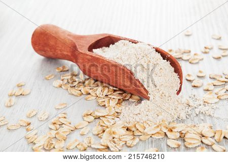 Oat wholegrain flour in spoon with oat flakes on wooden table. Gluten - free concept.