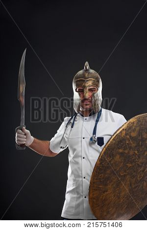 Studio shot of a medical male worker wearing uniform and a helmet posing with a shield and medieval sword fighting unhealthy and diseases healthcare medicine confidence experience warrior concept.