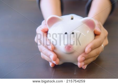 Piggy bank in hand on wooden top table money savings concept.
