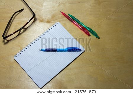 notebook, glasses and multicolored pens on a wooden background